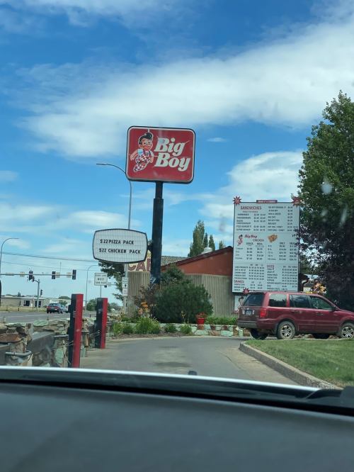 Sign for Big Boy restaurant with menu board visible, set against a blue sky and green landscaping.