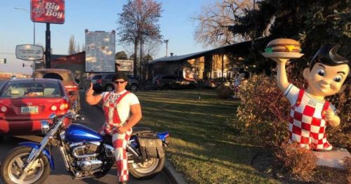 A man in a Big Boy costume poses on a motorcycle next to a large Big Boy statue outside a restaurant.