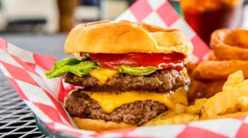 A juicy double cheeseburger with lettuce and ketchup, served with fries and onion rings in a red-checkered basket.