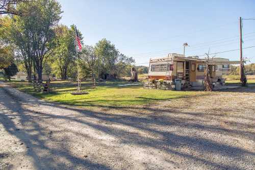 A gravel road leads to a campsite with two RVs, surrounded by trees and a clear blue sky.