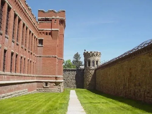 A view of a historic brick prison with a tower and grassy pathway under a clear blue sky.