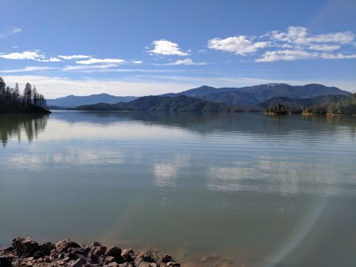 A serene lake surrounded by mountains under a clear blue sky, with calm water reflecting the landscape.