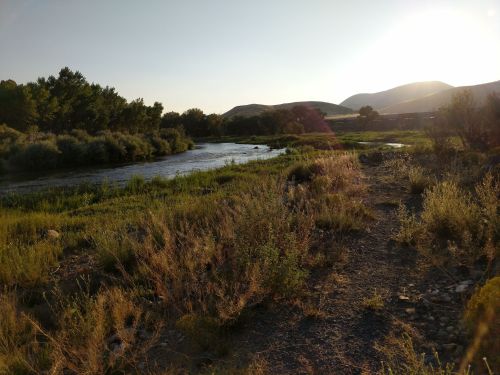 A serene river flows through a lush landscape, surrounded by greenery and mountains under a warm sunset.