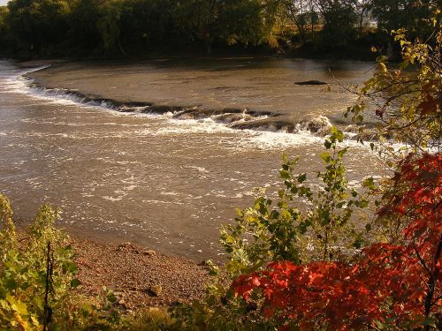 A serene river scene with gentle waves, surrounded by trees and colorful autumn foliage.