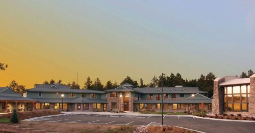 A modern building with a stone facade, surrounded by trees, under a colorful sky at dusk.