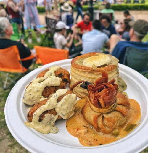 A plate of gourmet food featuring pastries, sauces, and garnishes, with people socializing in the background.