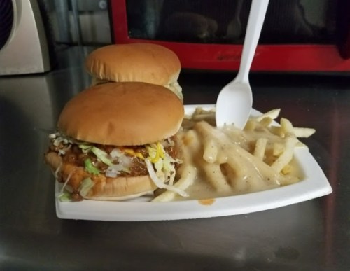 Two sandwiches with lettuce on a plate next to a serving of fries topped with gravy and a plastic spoon.