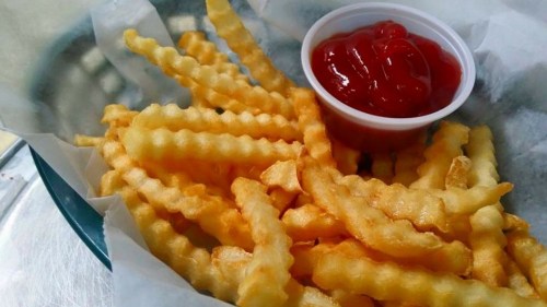 A serving of crinkle-cut fries with a small cup of ketchup on a paper-lined plate.
