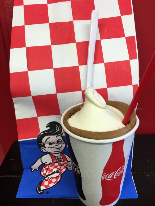 A cup of soft serve ice cream with a cookie crust, accompanied by a red and white checkered bag featuring a cartoon character.