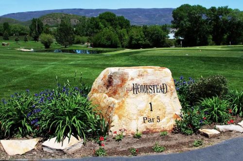 A large rock marker labeled "Homestead" with "1 Par 5" in a lush green golf course setting.
