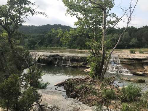 A serene landscape featuring a small waterfall, lush greenery, and a calm river surrounded by rocky terrain.