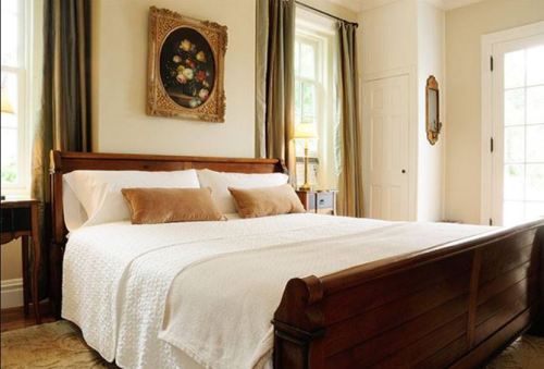 Cozy bedroom featuring a wooden bed, white bedding, and elegant decor with a floral painting on the wall.