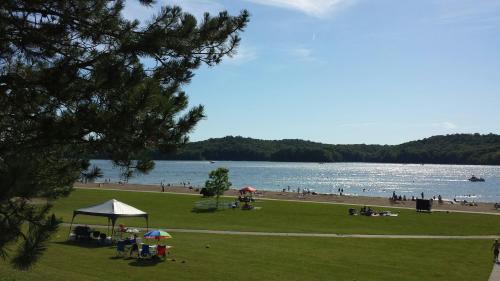 A sunny beach scene with people swimming, a grassy area, and a tent by the water, surrounded by hills.
