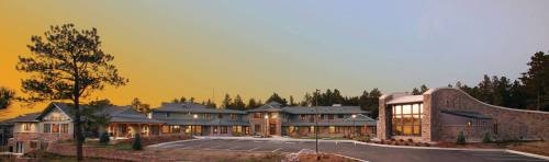 A modern building complex surrounded by trees, featuring a mix of stone and wood architecture at sunset.