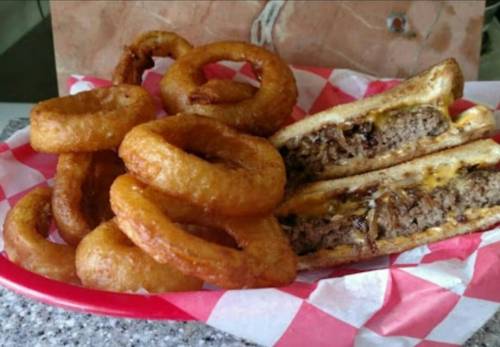 A plate of crispy onion rings next to a sliced meat-filled sandwich on a red and white checkered paper.