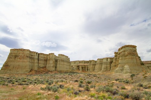 A panoramic view of rugged rock formations under a cloudy sky, surrounded by sparse vegetation.