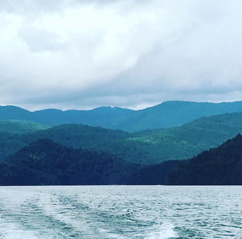 A serene lake surrounded by lush green mountains under a cloudy sky.