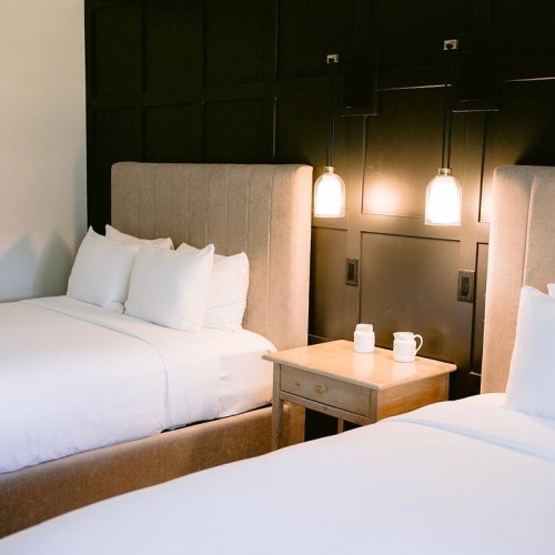 A cozy hotel room with two beds, a bedside table, and stylish wall lighting.