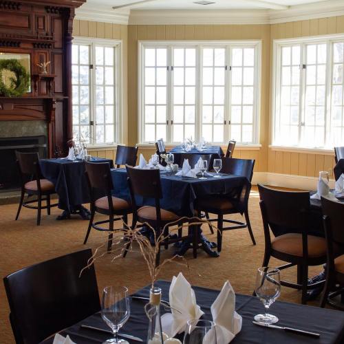 A cozy dining room with tables set for a meal, featuring large windows and a fireplace.