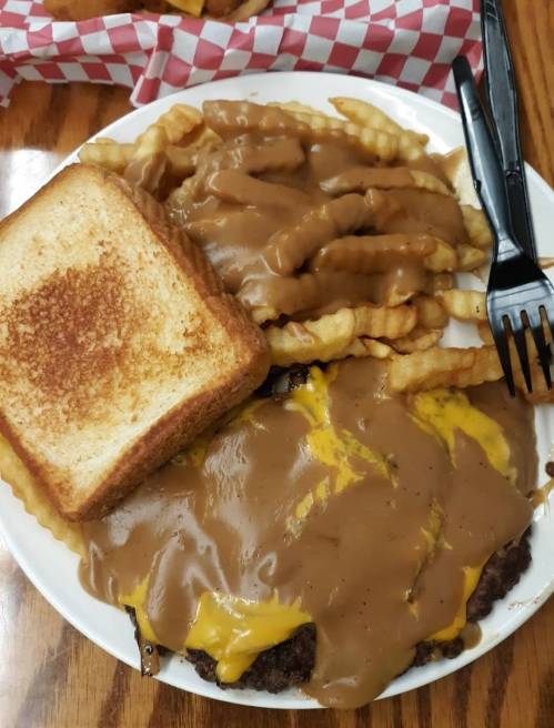 A plate featuring a cheeseburger topped with gravy, crinkle-cut fries smothered in gravy, and a slice of toasted bread.