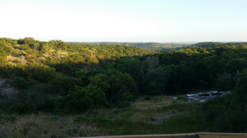 A scenic view of lush green hills and trees under a clear sky, with a hint of distant landscape in the background.