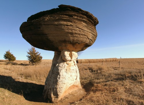A large, mushroom-shaped rock formation stands in a grassy landscape under a clear blue sky.