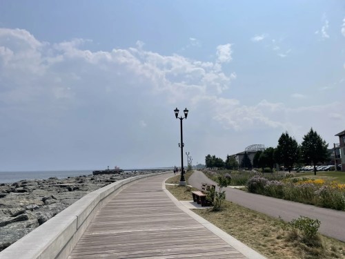A scenic waterfront path lined with lampposts, rocks, and greenery under a cloudy sky.