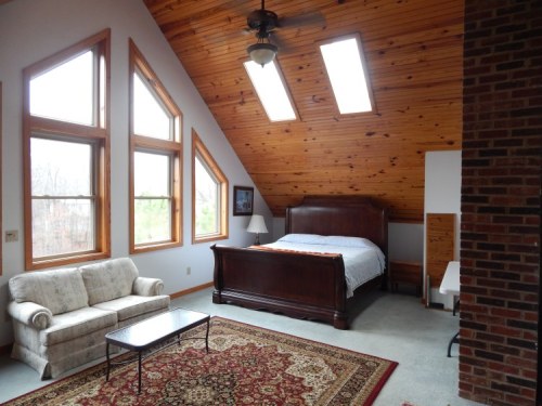 Cozy attic bedroom with a wooden bed, large windows, a sofa, and a patterned rug.