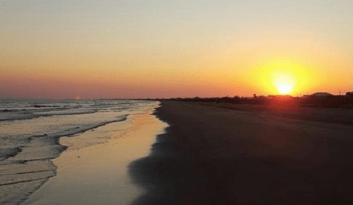 A serene beach at sunset, with gentle waves lapping at the shore and a vibrant orange sun on the horizon.