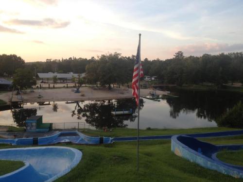 A view of a lake with a flag in the foreground, surrounded by trees and a sandy area at sunset.