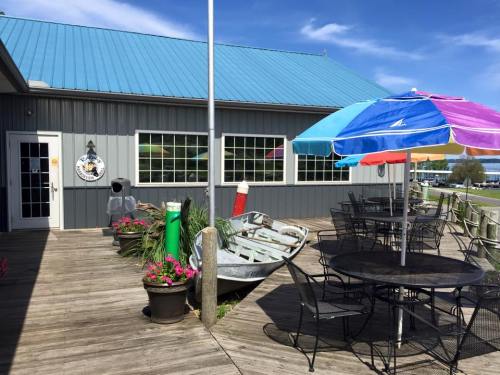 A wooden deck with a colorful umbrella table, an old boat, and a building with large windows under a blue sky.