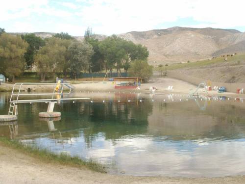 A serene lake with a diving board, sandy beach, and distant hills under a cloudy sky.