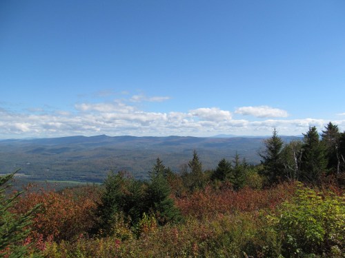 A panoramic view of rolling mountains and colorful autumn foliage under a clear blue sky.