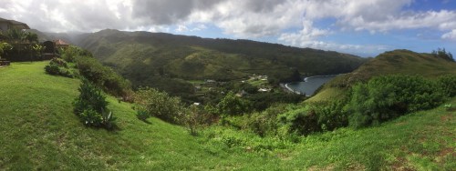 A panoramic view of lush green hills and a coastal bay under a partly cloudy sky.