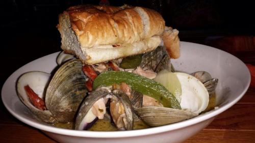 A bowl of clams and vegetables topped with a piece of bread, served in a savory broth.