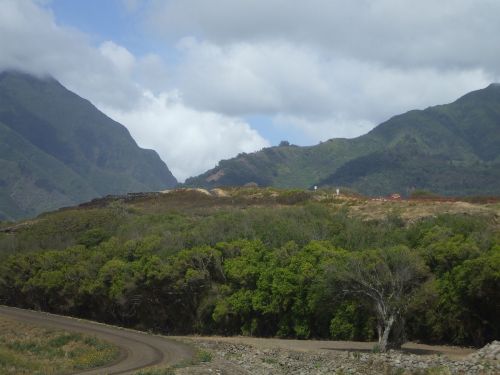 A scenic view of mountains under a cloudy sky, with a winding road and lush greenery in the foreground.