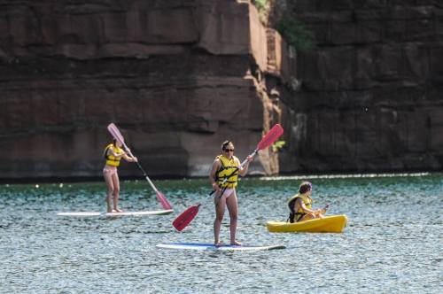 Three people paddleboarding and kayaking on a calm lake surrounded by rocky cliffs.
