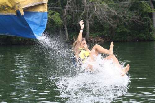 A person in a life jacket is falling into the water, creating a splash, with trees in the background.