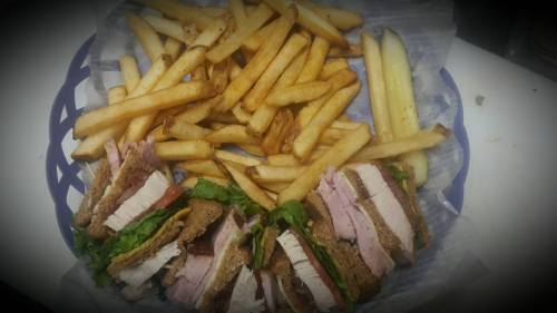 A basket of crispy fries alongside a stacked sandwich with layers of turkey, lettuce, and tomato.