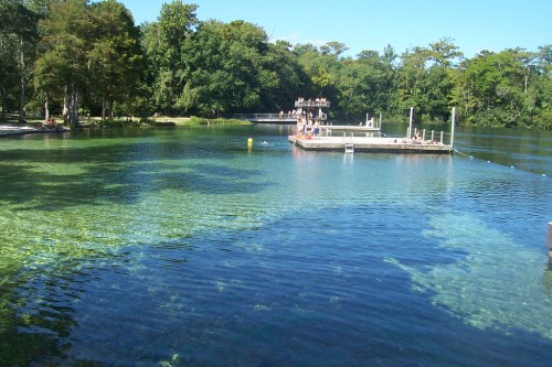 A serene lake with clear water, surrounded by trees, featuring a dock and people enjoying the scenery.