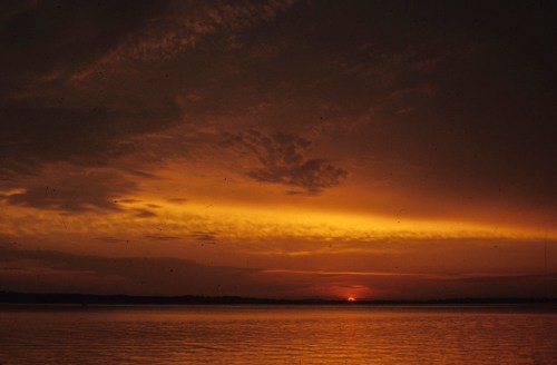 A serene sunset over a calm lake, with vibrant orange and yellow hues reflecting on the water.