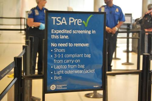 Sign for TSA PreCheck lane, listing items not required to remove: shoes, compliant bag, laptop, light outerwear, and belt.
