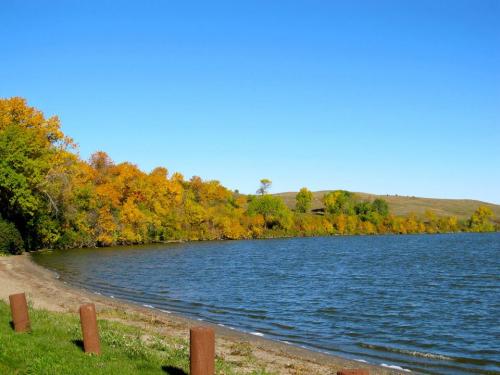 A serene lakeside view with colorful autumn trees and a clear blue sky.