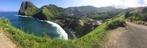 Panoramic view of a coastal landscape with lush green hills, a winding road, and a serene blue ocean.