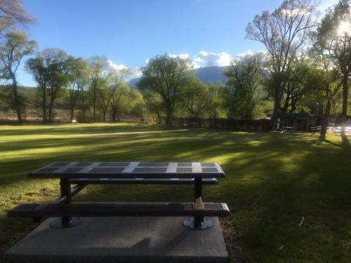 A picnic table in a grassy park, surrounded by trees and mountains under a clear blue sky.