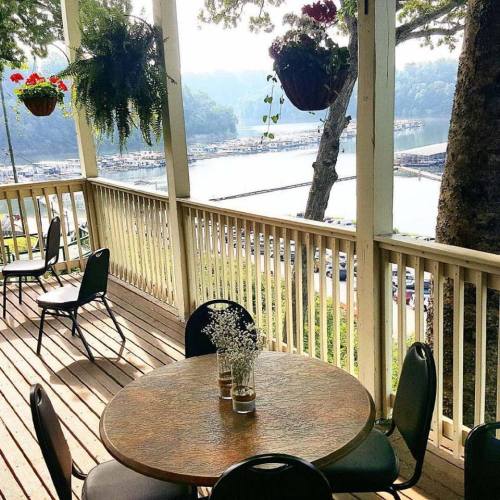 A cozy outdoor seating area with a round table and chairs, overlooking a marina and lush greenery.