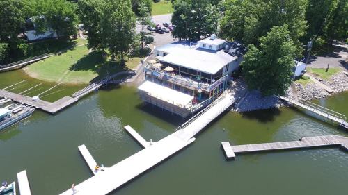 Aerial view of a lakeside building with a deck, surrounded by water and greenery, with docks for boats nearby.
