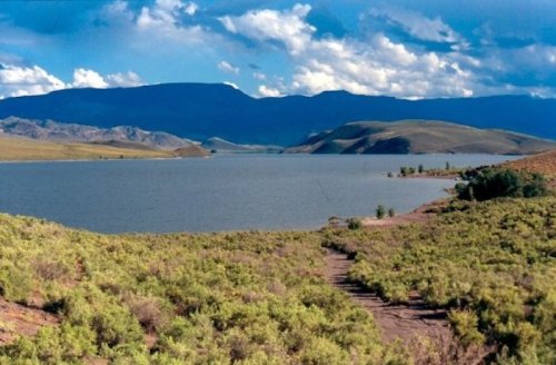 A serene landscape featuring a lake surrounded by rolling hills and lush greenery under a partly cloudy sky.