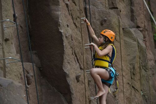 A child in a helmet climbs a rocky wall using metal grips, showcasing determination and adventure.