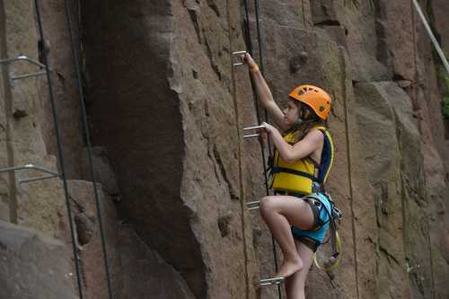 A child in a helmet climbs a rocky wall using metal grips, showcasing determination and adventure.